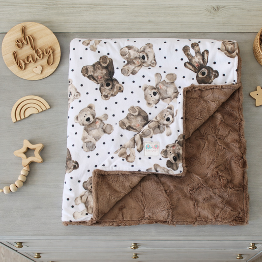 Baby blanket with teddy bear pattern on a wooden surface with baby toys.